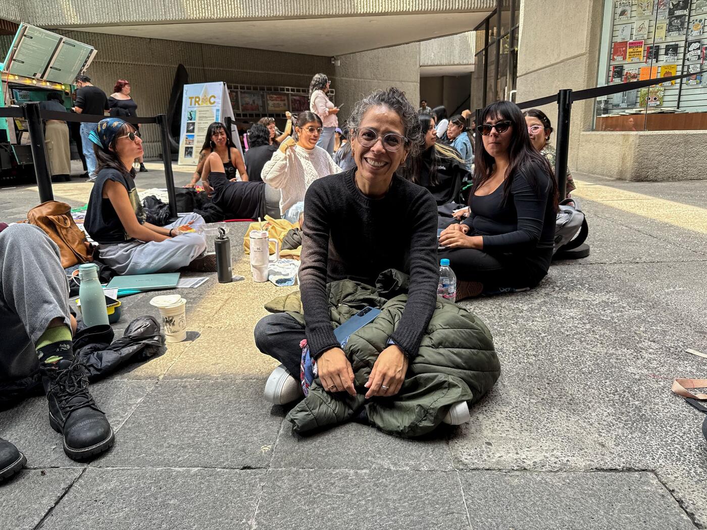 Mirna Estrella sentada en el suelo, sonriendo, en la fila de espera.