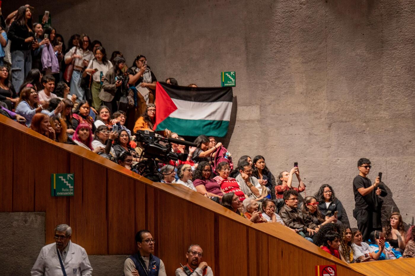 Asistentes en las gradas despliegan una bandera de Palestina.