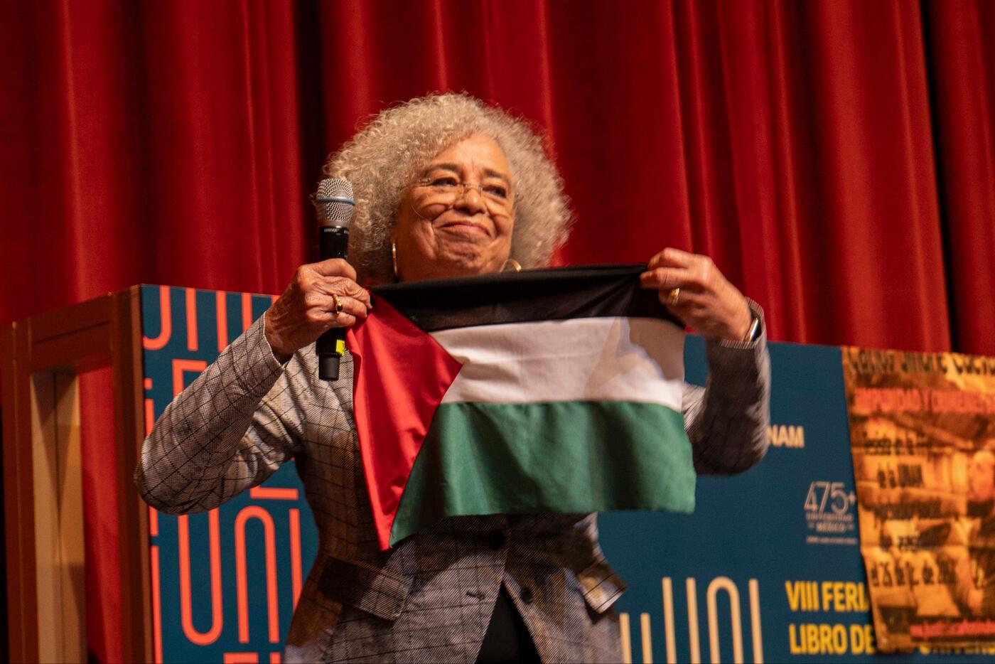 Angela Davis sostiene una bandera de Palestina en el escenario.
