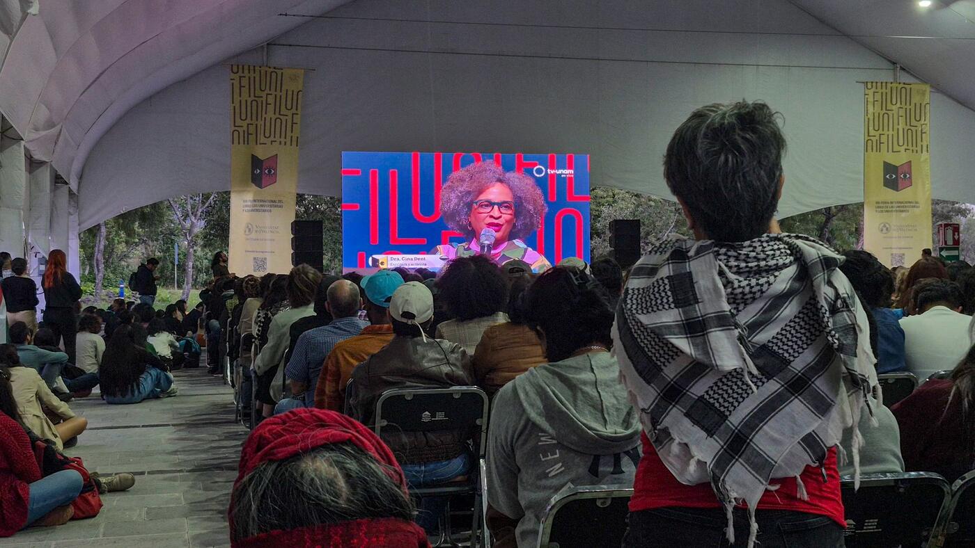 Personas de espaldas miran la transmisión en una pantalla bajo una carpa.