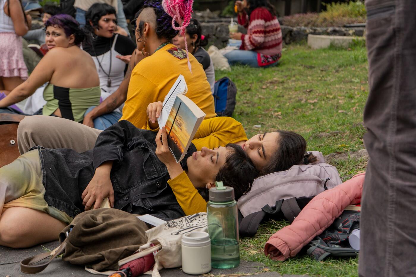 Dos jóvenes recostadas en el pasto leen mientras esperan.